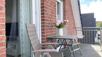 Een balkon met een tafel, twee stoelen, een bloempot en een raam met gordijn.