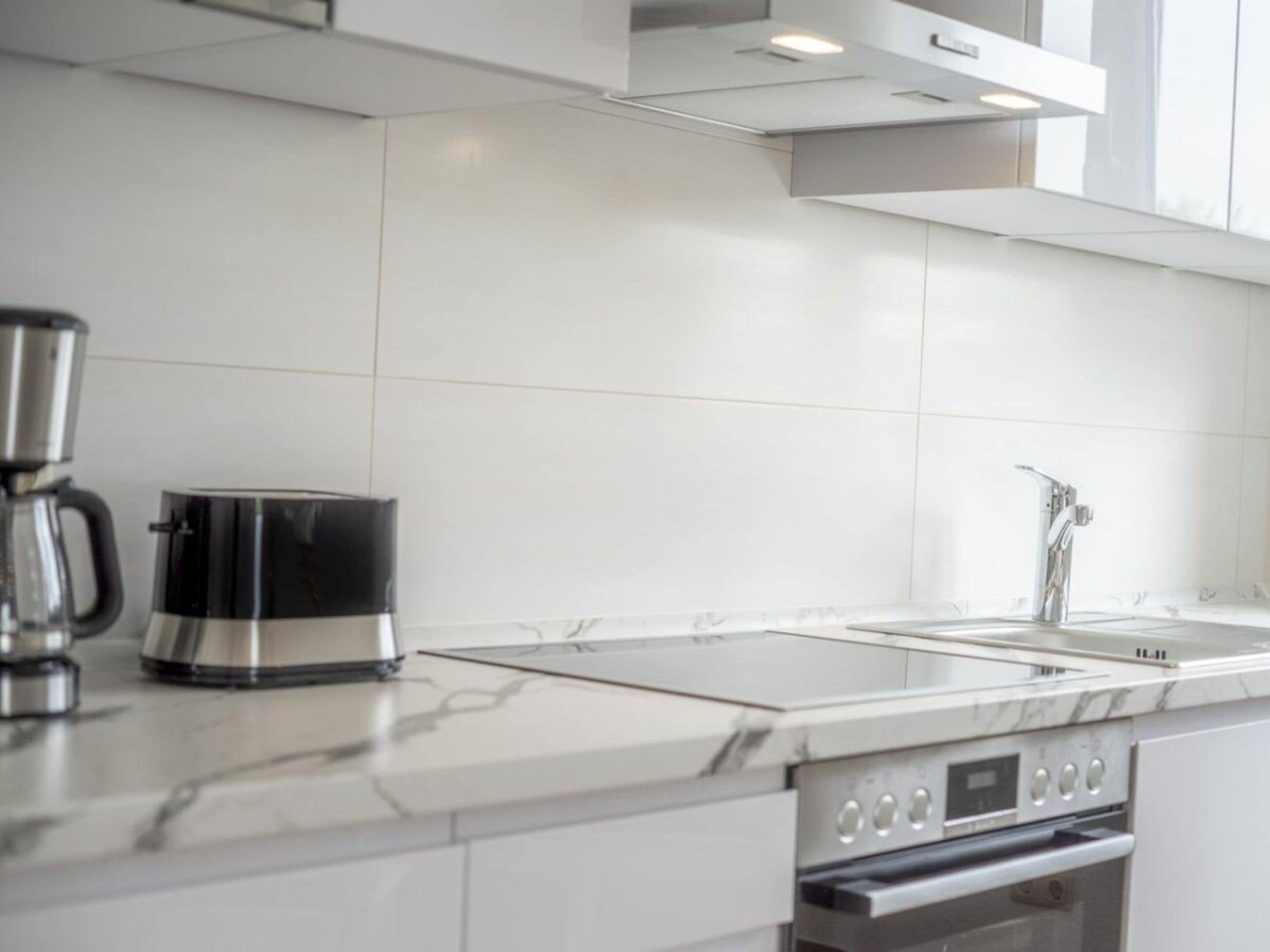 Una cocina moderna con cafetera de acero inoxidable, horno empotrado y un lavabo.