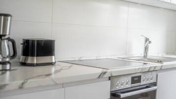 Una cocina moderna con cafetera de acero inoxidable, horno empotrado y un lavabo.