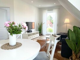 Una sala de estar moderna con una mesa redonda blanca, un televisor de pantalla plana, un sofá negro y una planta en maceta.