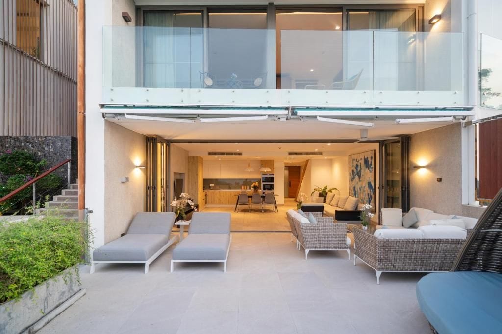 Una casa moderna con balcón de vidrio, comedor y sala de estar con sofás y una mesa de centro.