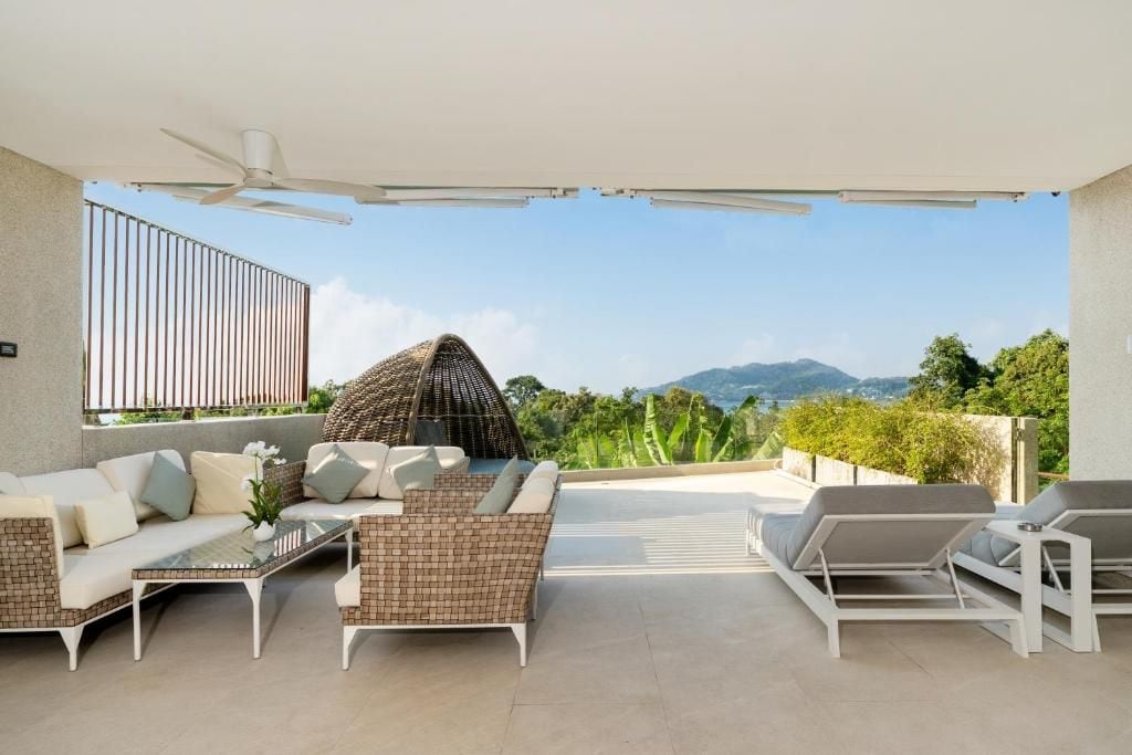 Amplia zona de estar al aire libre con sofás, una mesa de comedor y sillones, con vistas a un paisaje montañoso.