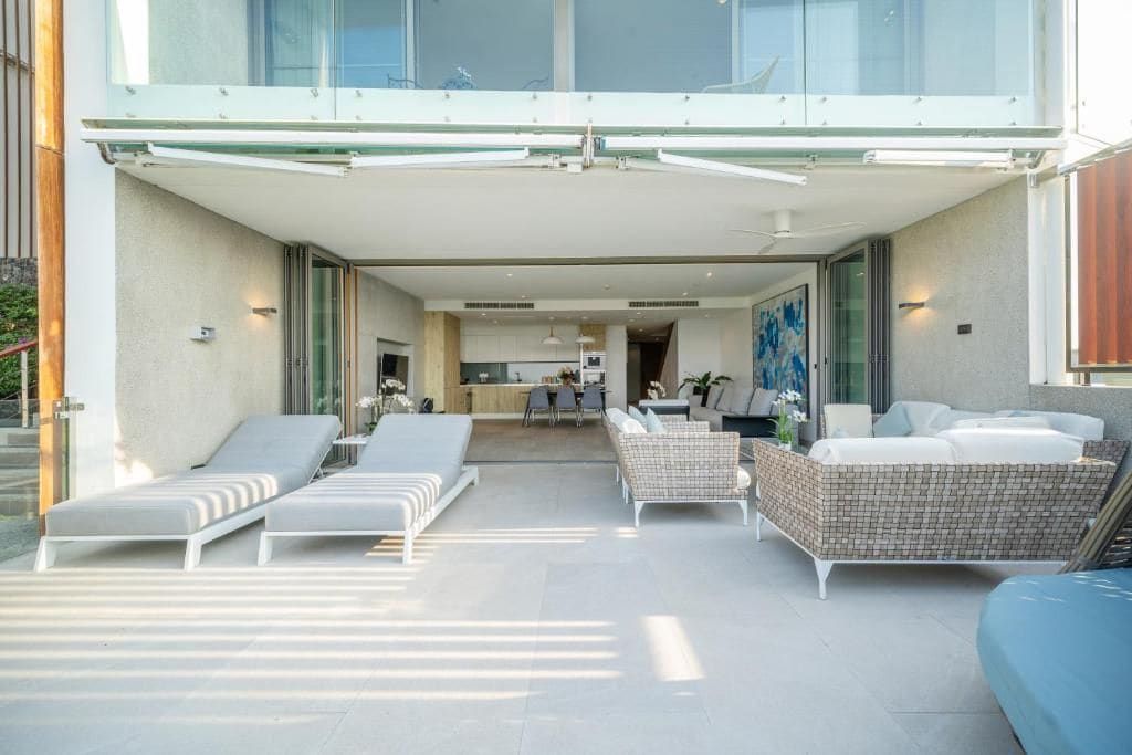 A modern outdoor living area with lounge chairs, a wicker sofa, and a kitchen in the background.
