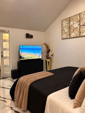 Ein Schlafzimmer mit einem Bett, einem Fernseher auf einer Kommode, einer Vase mit Trockenblumen und einem Gemälde an der Wand.