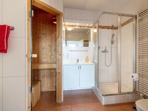 A bathroom with a glass shower enclosure, a white sink, and a wooden door. - Holiday Apartment With 2 Bedrooms (Grossenbrode)