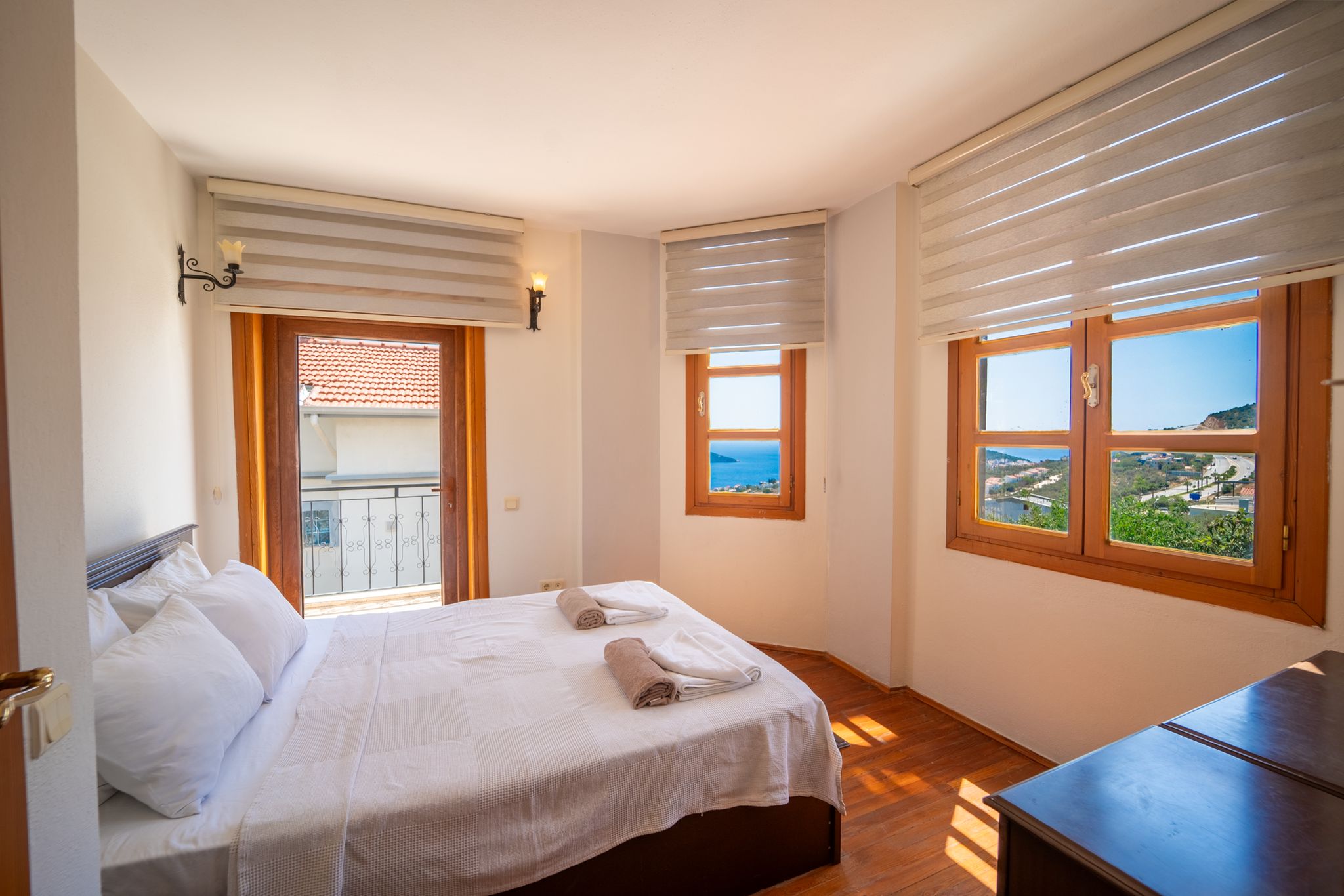 Ein Schlafzimmer mit einem Bett, zwei Fenstern, einer Balkontür und Meerblick.