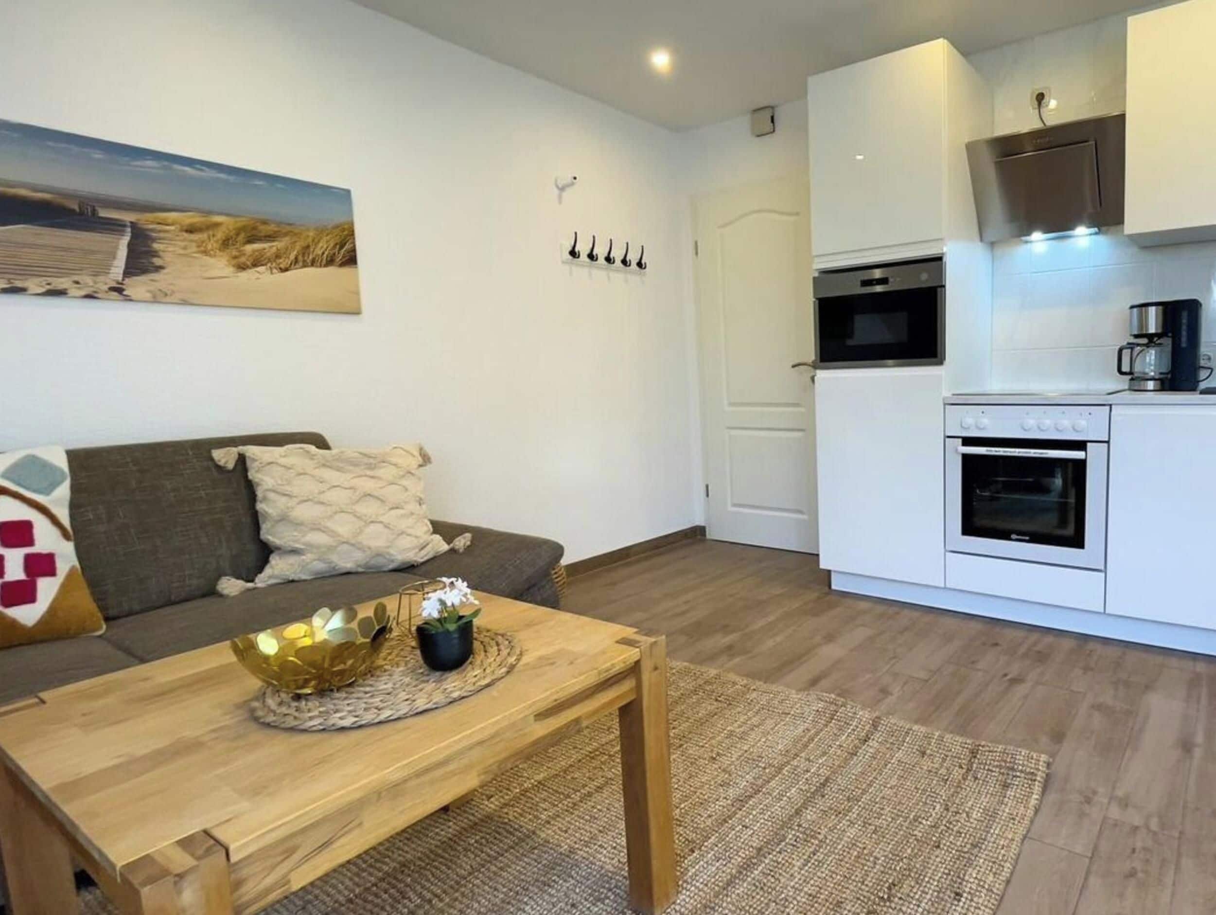 Un espace de vie compact comprenant un canapé, une table basse, un coin cuisine avec une cuisinière et un four, et une porte.