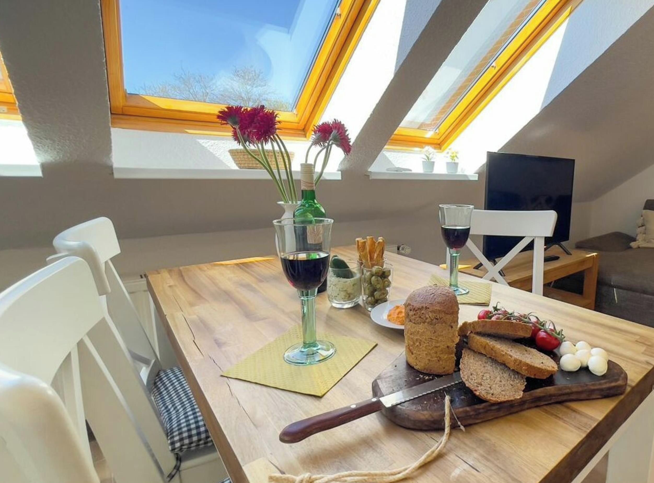 Un comedor con una mesa dispuesta para dos personas, una botella de vino, un vaso de agua, un plato de pan y un cuchillo.