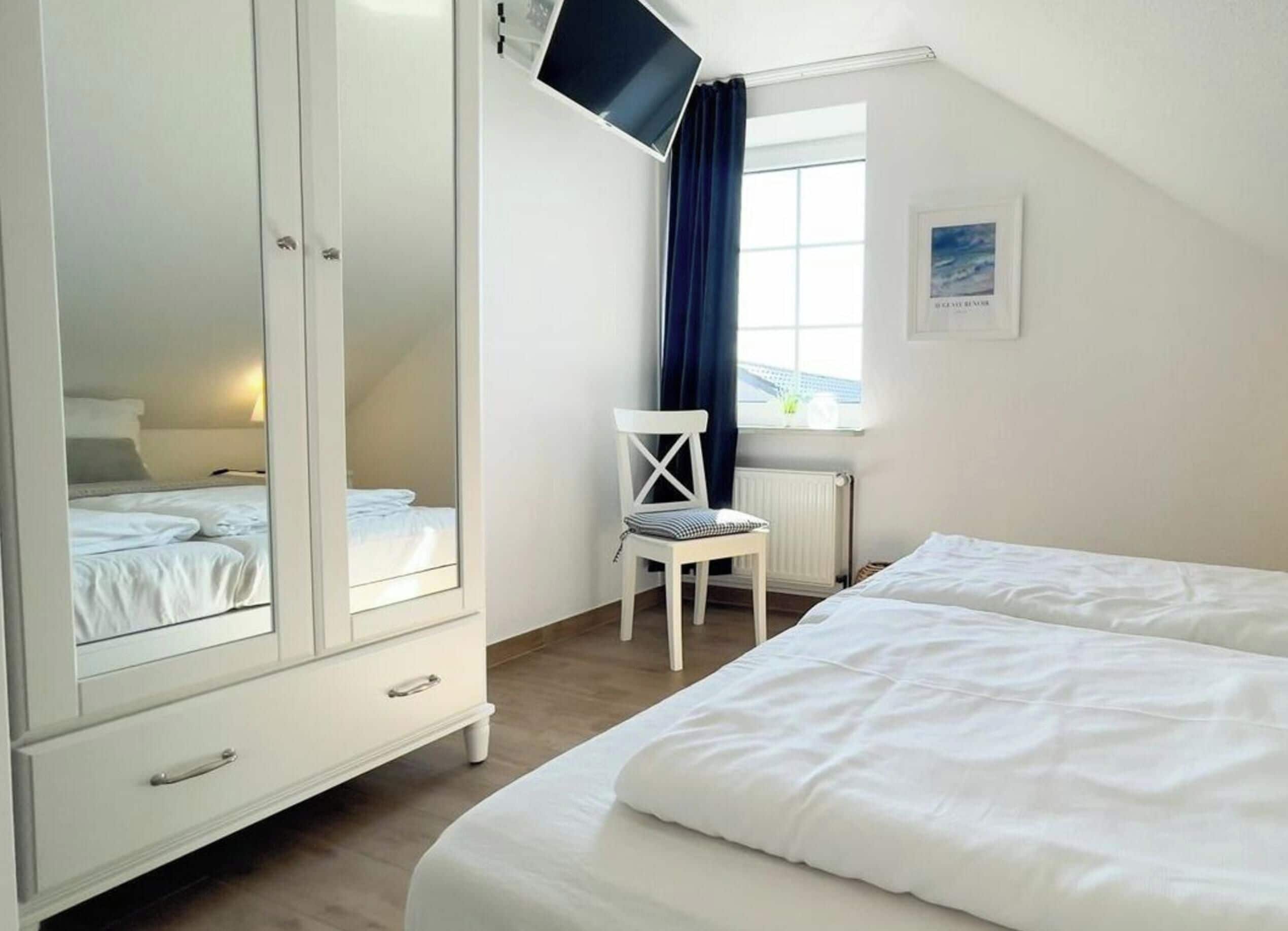 Un dormitorio con dos camas, un armario blanco, una silla, un televisor y una ventana con cortinas.