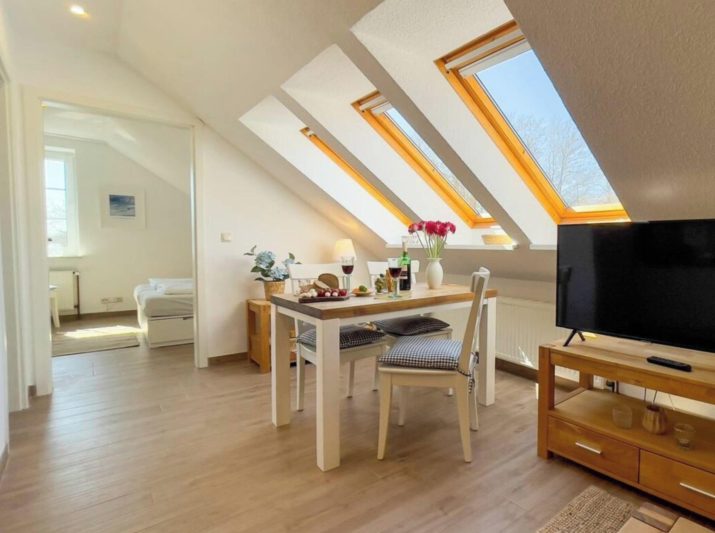 A room with a dining table, chairs, a TV, and a skylight.