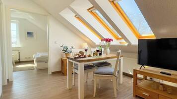 A room with a dining table, chairs, a TV, and a skylight.