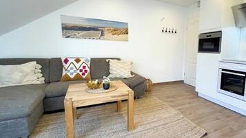 A living room with a sofa, a coffee table, a painting, a coat rack, and a built-in oven.