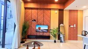 A modern living room with a flat-screen TV mounted on a wooden wall, a glass coffee table, and two potted plants. - Trion KL Premier Residence (Kuala Lumpur)