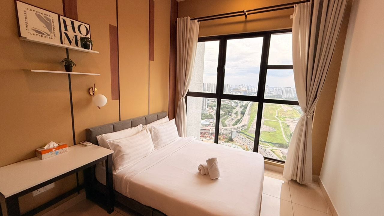 A hotel room with a bed, a bedside table, a window with curtains, and a view of the cityscape.