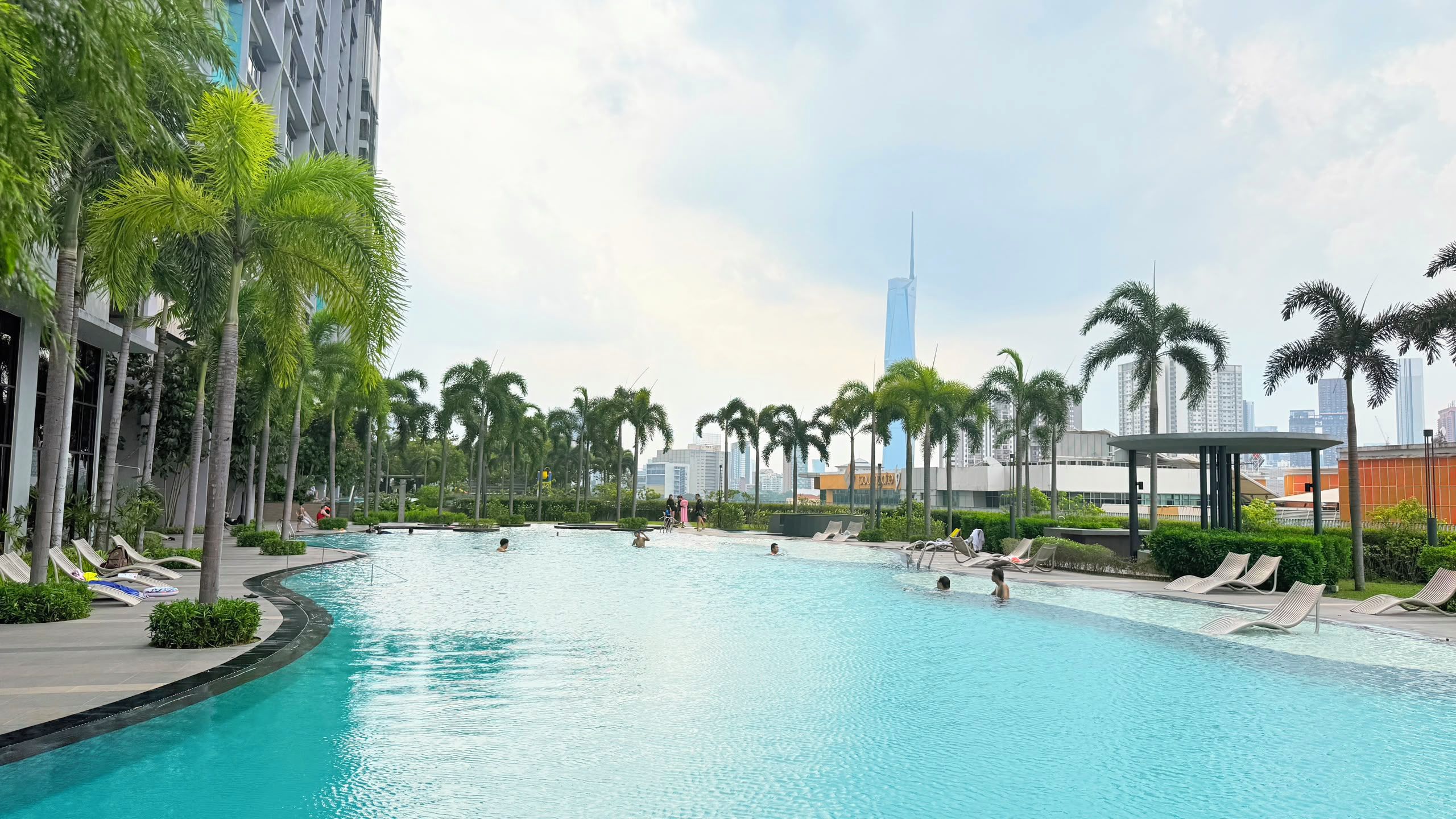 A swimming pool with lounge chairs and palm trees, surrounded by modern buildings.