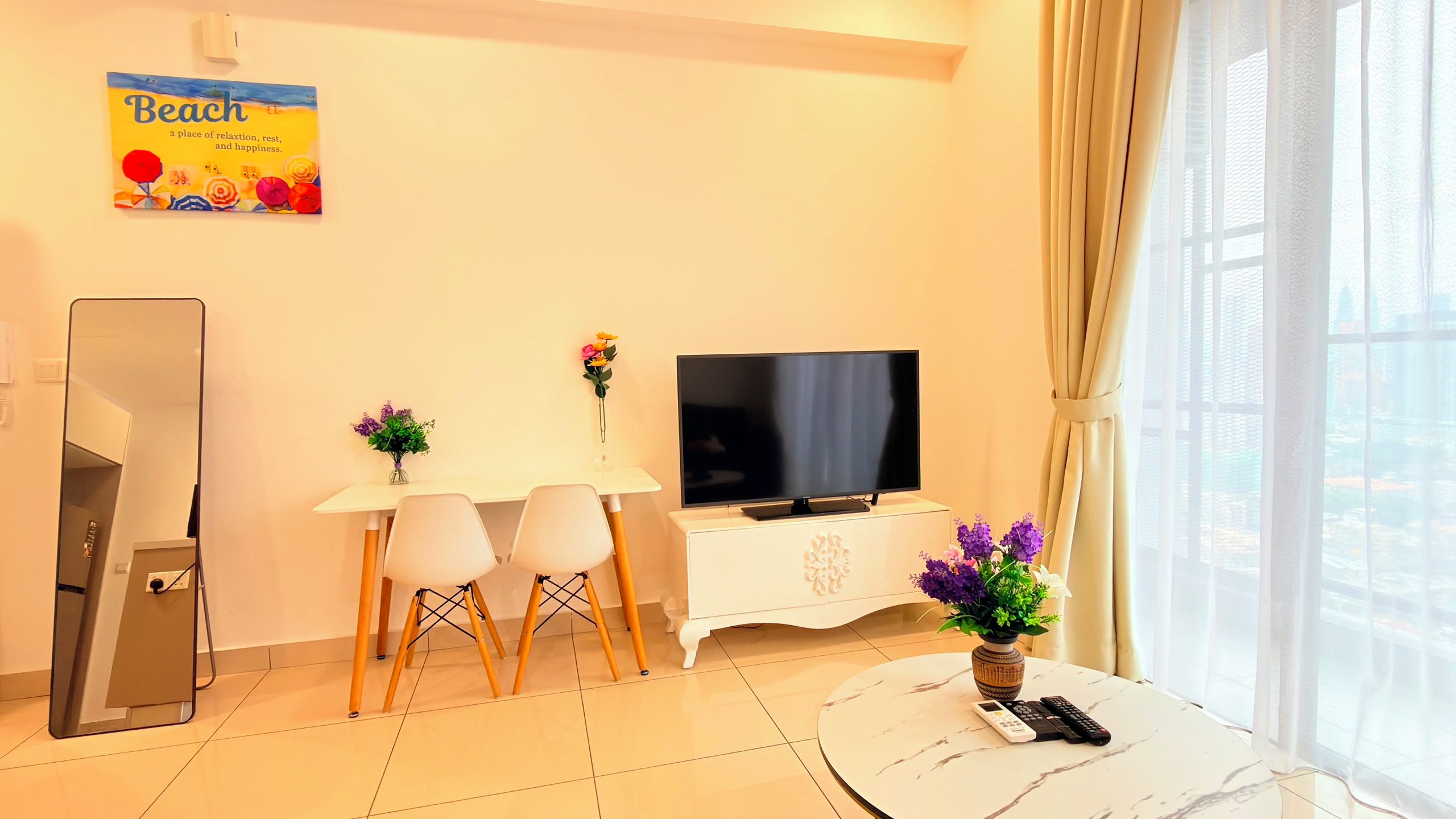 A modern living room with a flat-screen TV, a dining area with two chairs, a coffee table, and a potted plant.