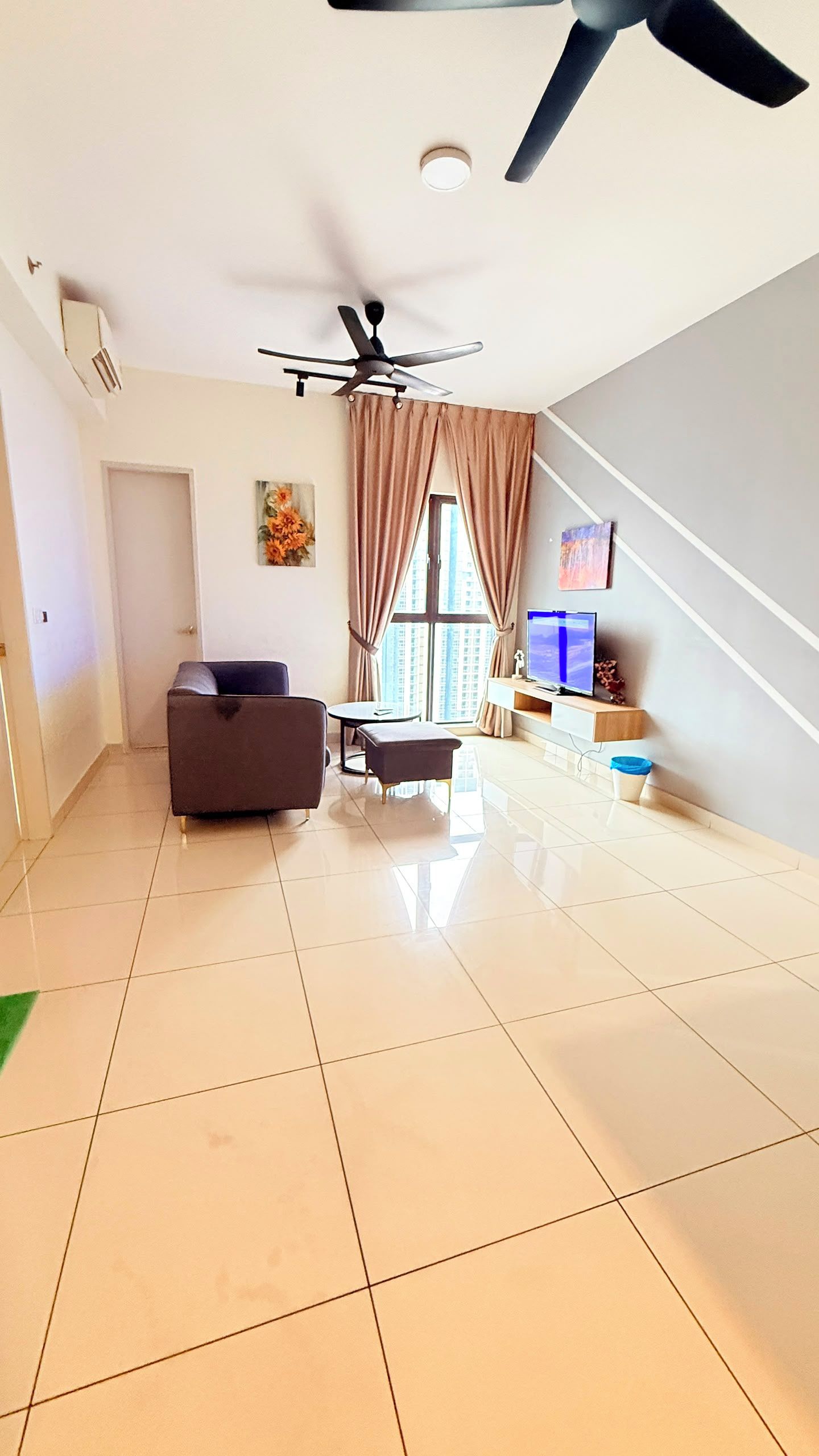 A spacious living area with a ceiling fan, a sofa, a coffee table, a TV on a wooden stand, and a window with curtains.