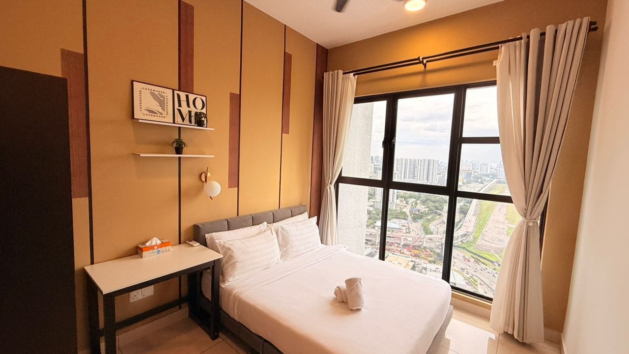 A hotel room with a bed, a bedside table, a window with curtains, and a city view.