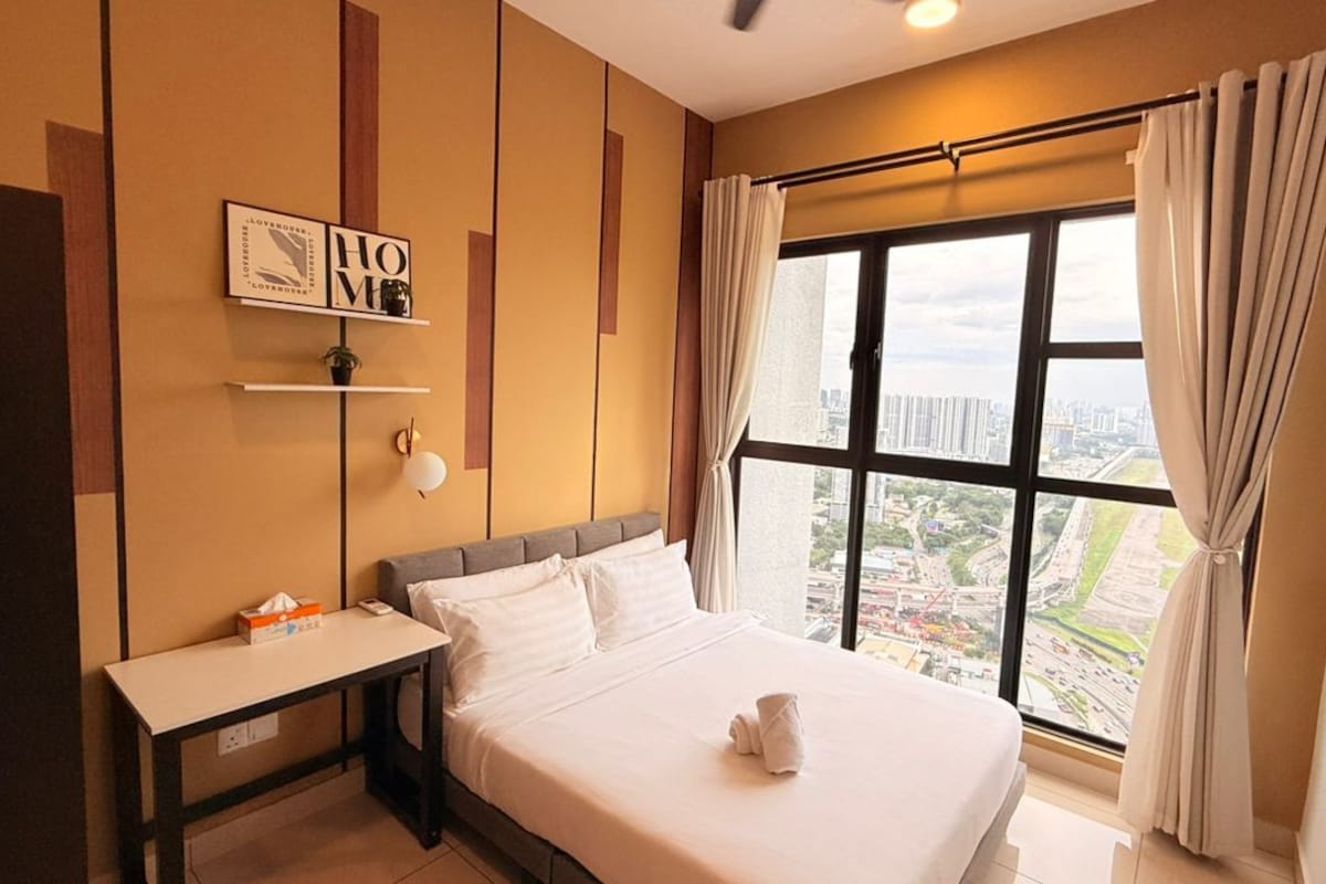 A hotel room with a bed, a bedside table, a window with curtains, and a city view.