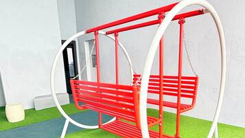 A red swing set with white supports and chains, located on a green artificial turf area.