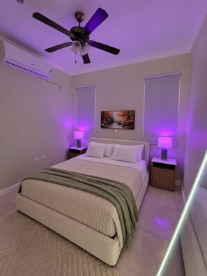 Ein Schlafzimmer mit einem Bett, Nachttischen, einem Deckenventilator und einem Bild an der Wand.
