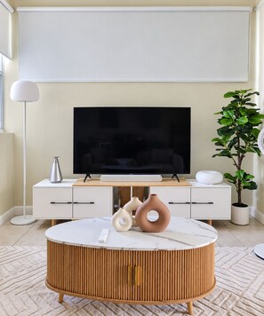 Ein modernes Wohnzimmer mit einem Flachbildfernseher, einem runden Couchtisch und einer Topfpflanze.