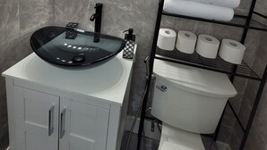 Un baño con un espejo redondo, un lavamanos negro, un inodoro y un perchero con toallas dobladas.