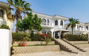 A multi-story building with a white facade, arched windows, and a balcony. - Classic Beachfront Villa w Pool on Palm Jumeirah (Dubai)
