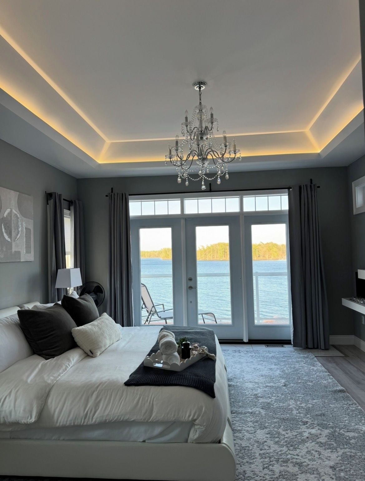 Une chambre à coucher avec un grand lit, un lustre, une vue sur l’eau et une porte donnant sur un espace extérieur.