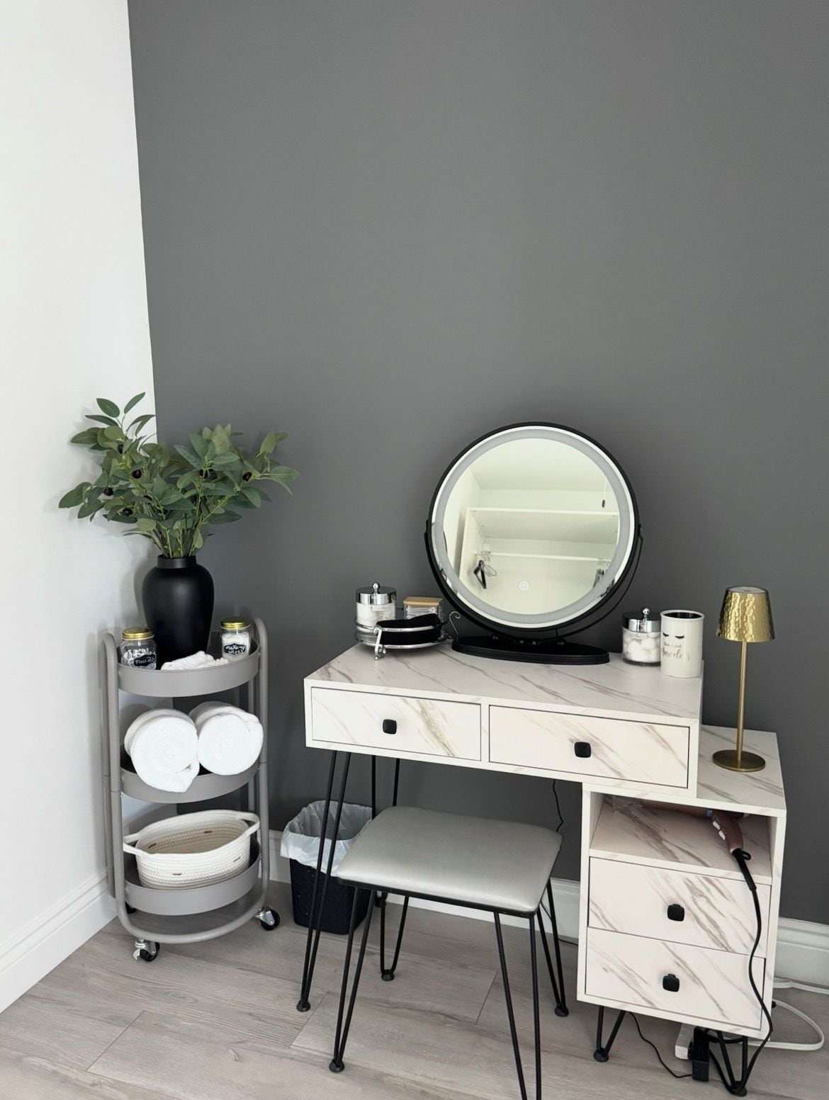 Une coiffeuse avec un miroir rond, une plante et une étagère contenant des articles de toilette.