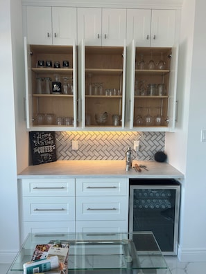 A kitchen with white cabinets, a coffee-themed sign, and a glass coffee machine.