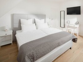Un dormitorio moderno con una cama grande, mesitas de noche blancas, un escritorio y un televisor de pantalla plana en la pared.
