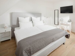 Un dormitorio moderno con una cama grande, mesitas de noche blancas, un escritorio y un televisor de pantalla plana en la pared.