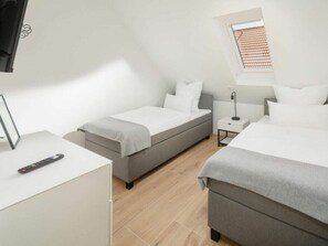 A modern hotel room with two beds, a desk, a TV, and a window. - Coastal Suite East Directly on the Waterfront (Krummhoern)
