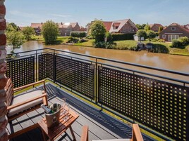Un balcón con vistas a un río, muebles de madera y una valla de metal.