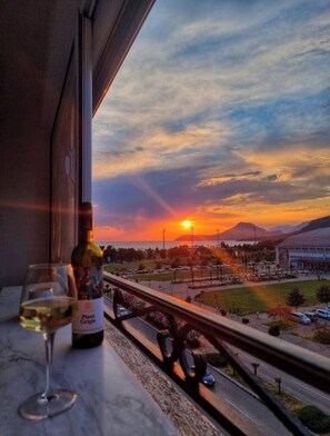 A sunset view from a balcony with a bottle of wine and a glass on the windowsill.