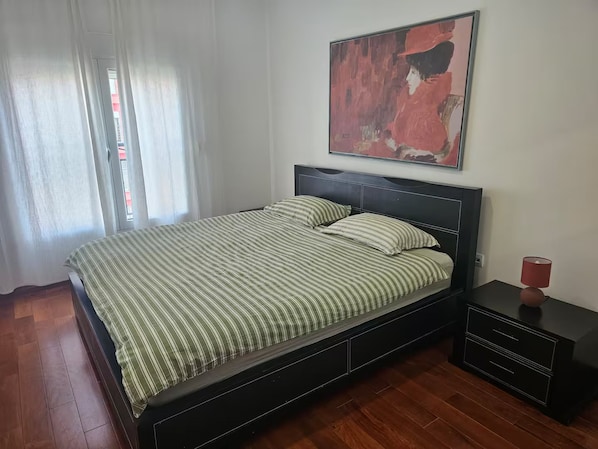 A bedroom with a bed, a nightstand, a lamp, and a painting on the wall.