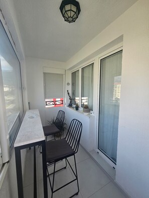 A balcony with a table and two chairs, a potted plant, and a window with a view of buildings.