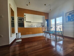 A modern kitchen with wooden cabinets, a dining area with metal chairs, and a balcony with a railing.