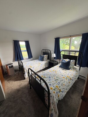 Un dormitorio con dos camas individuales, una mesita de noche con lámpara, un calentador y una ventana con cortinas.