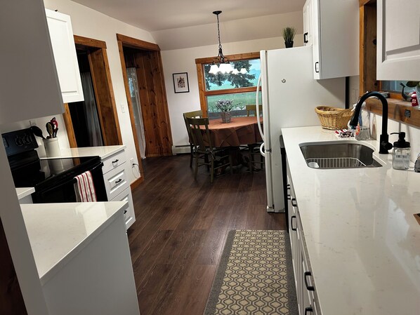 A kitchen with a dining area, wooden flooring, and a window with a view.