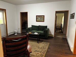 A living room with a green sofa, a wooden coffee table, a patterned rug, and a painting on the wall.