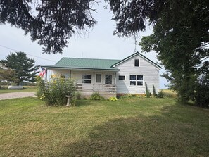 A single-story house with a green roof, a front porch, and a small garden with flowers.