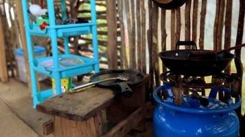 A rustic outdoor setting with a blue gas cylinder, a metal pot, and a blue plastic shelf.