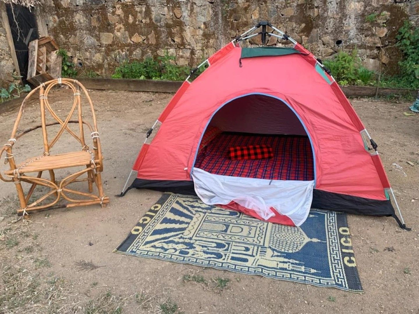 Una carpa roja con interior blanco, una silla tejida y un tapete estampado en el suelo.