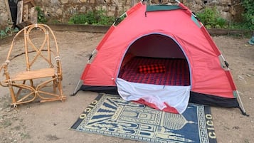 Una carpa roja con interior blanco, una silla tejida y un tapete estampado en el suelo.