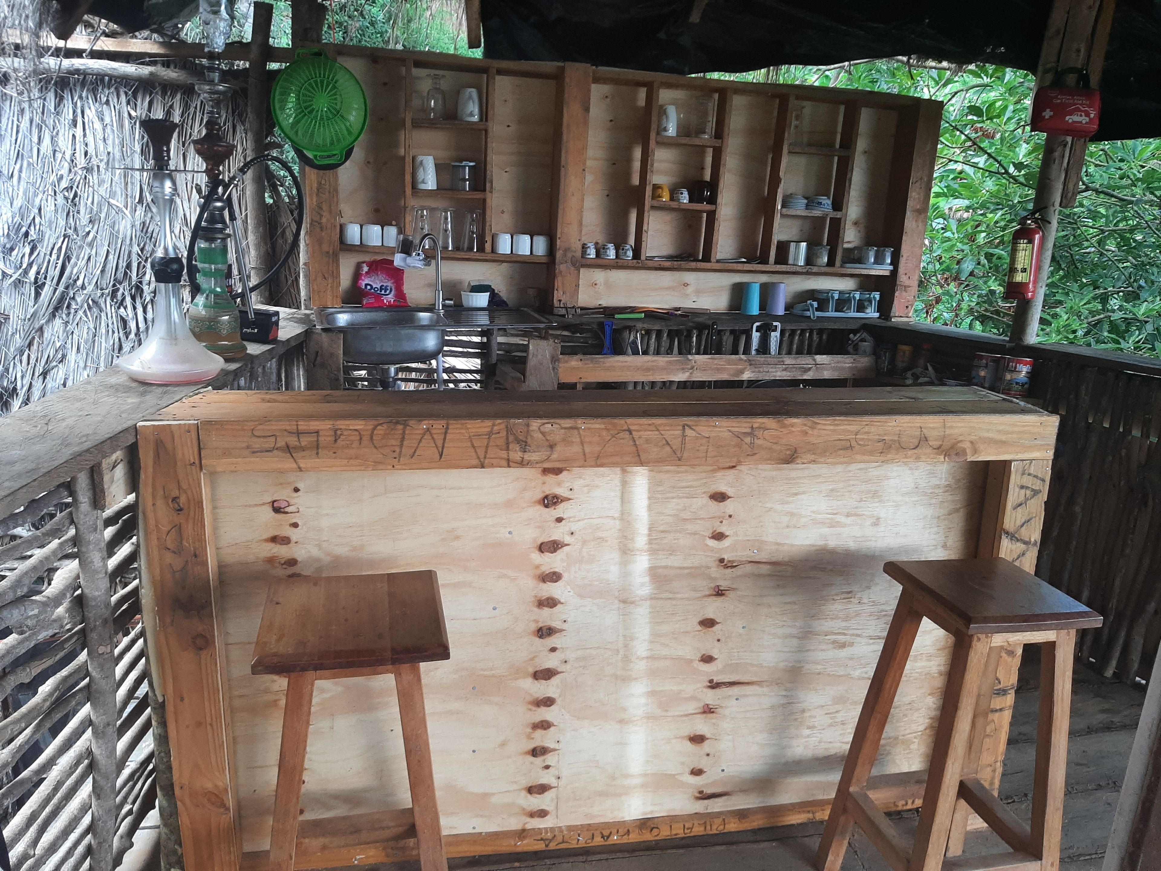 Eine Holztresorecke mit Hockern, einem Spülbecken und Regalen mit verschiedenen Gegenständen.