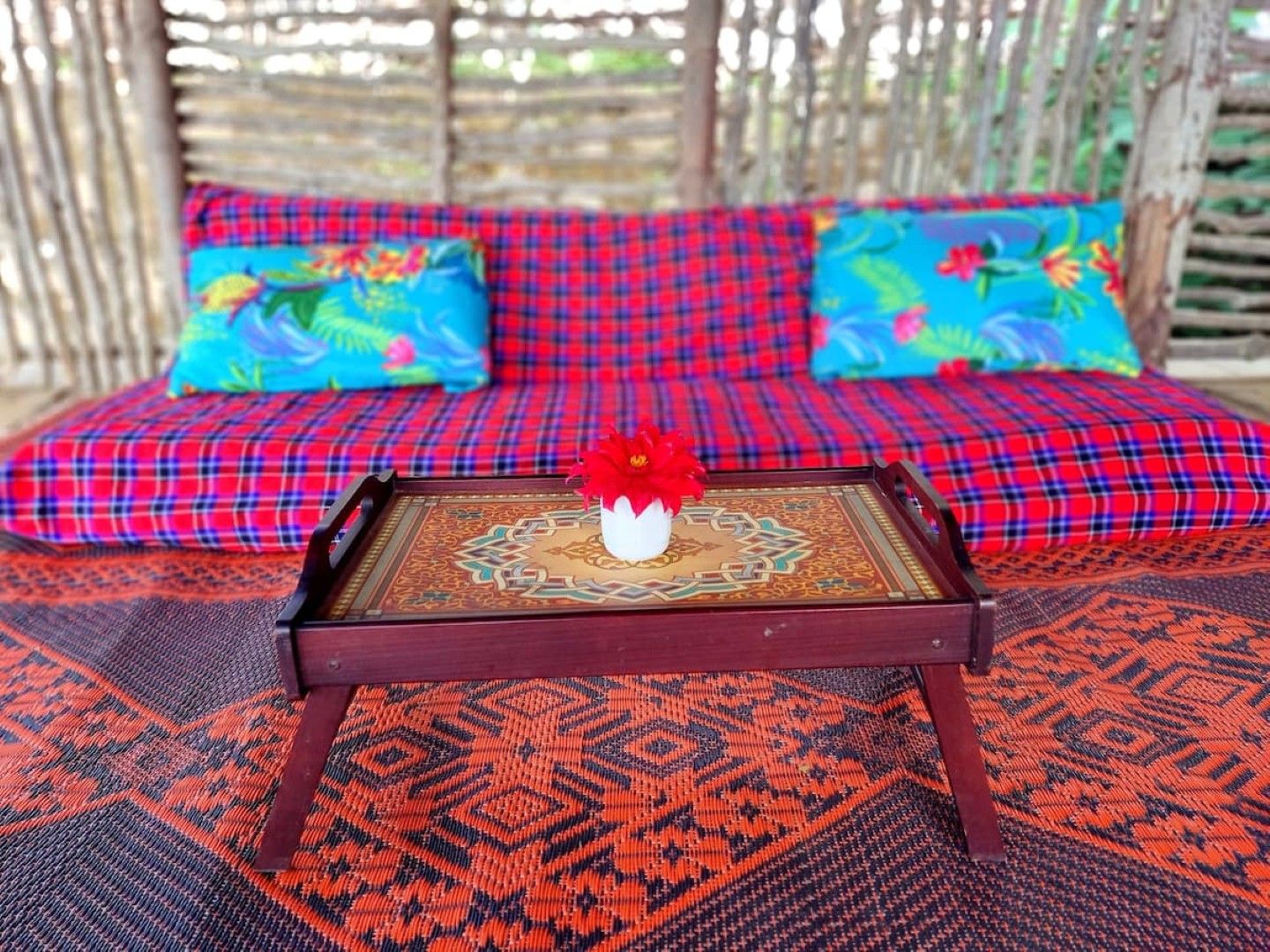 A sofa with a red and blue checkered pattern, a decorative tray with a floral centerpiece, and a patterned rug.