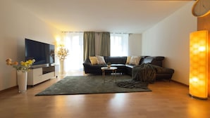 Uma sala de estar moderna com televisão de tela plana, um sofá, uma mesa de centro e um abajur decorativo.