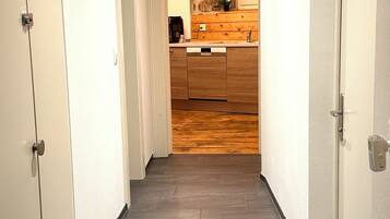 A hallway with a wooden floor leading to a kitchen area with a stone wall backsplash.